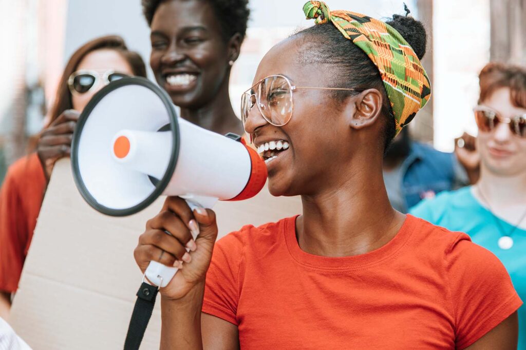 Young black woman holding a mircophone surrounded by a diverse group of young people