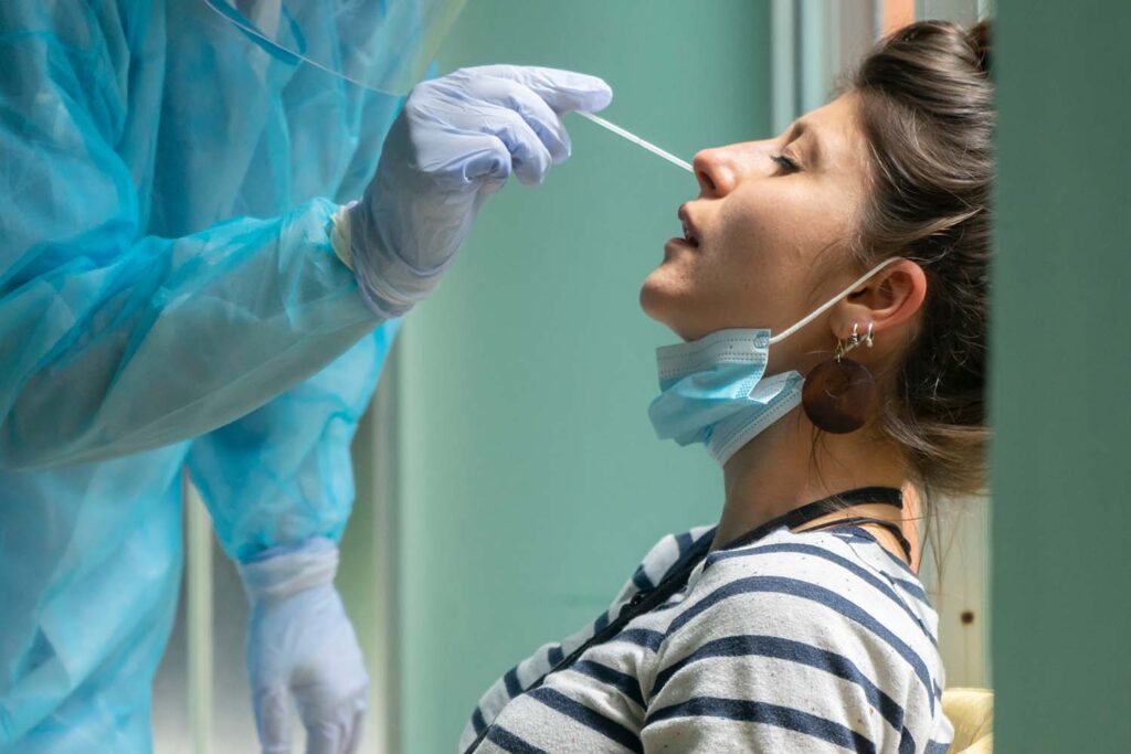 White woman receives COVID-19 test by heathcare worker in full protective equipment